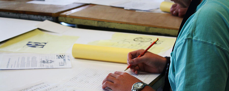 A close up of a male student working on his drawings in the classroom.