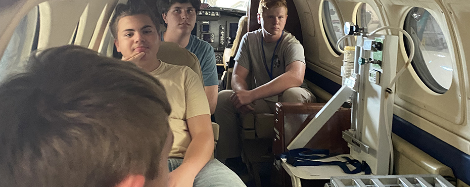 Four students sit inside a small airplane while on the ground.