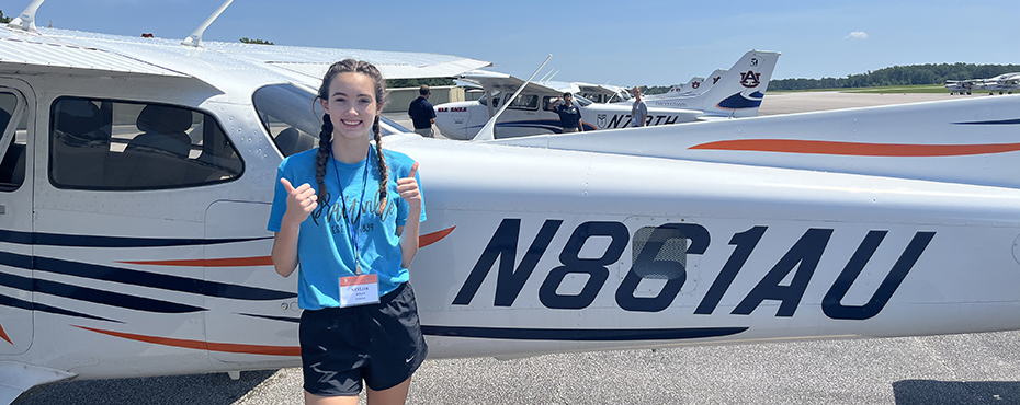 A female camper gives two thumbs up in front of a single-engine airplane at Auburn's Airport.