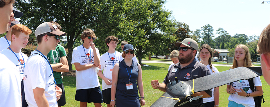 Students listen to an instructor as he holds and explains how to use a drone.