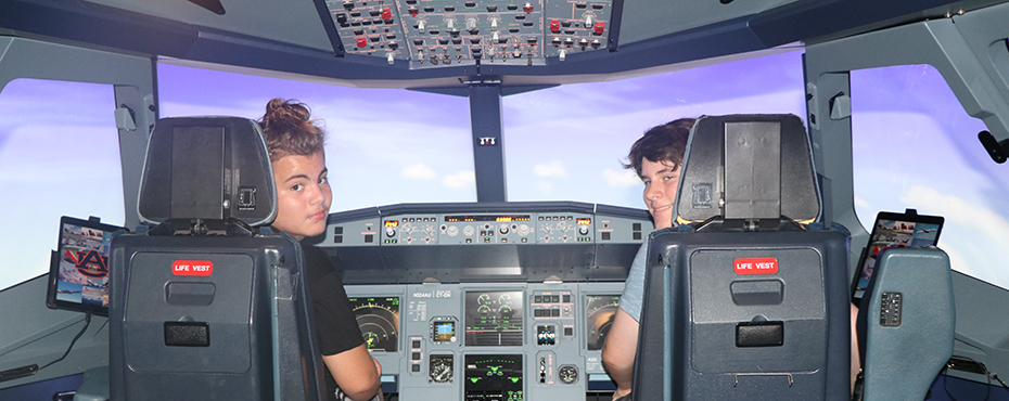 Two students look back and smile as they use a flight simulator.