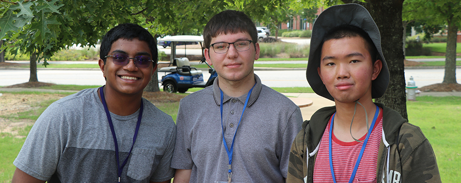 Three male campers smile for a photograph while outside on Auburn's Campus.