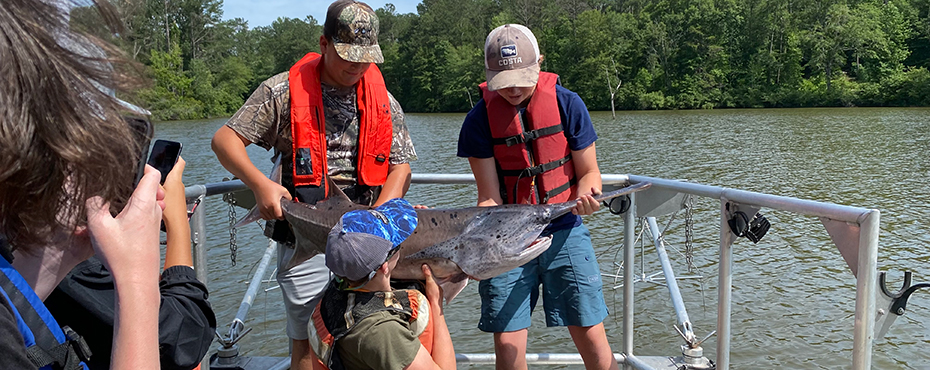 Students holding a big fish on a boat