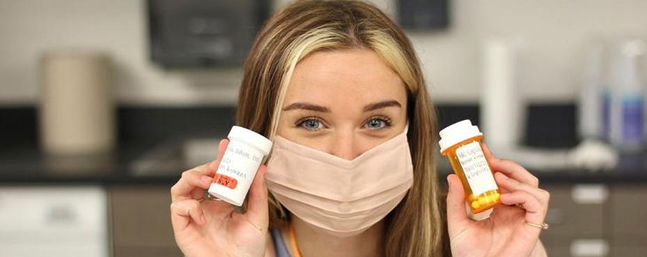 Girl wearing face mask holds up two pill bottles at Pharmacy camp.