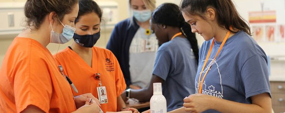 AU Nursing students wearing orange scrubs show camper how to administer shot.