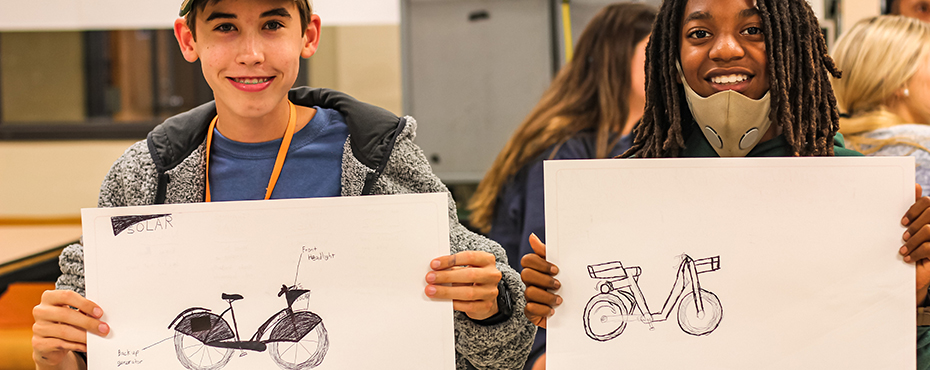 Two students hold up drawings of bicycles during industrial design camp.