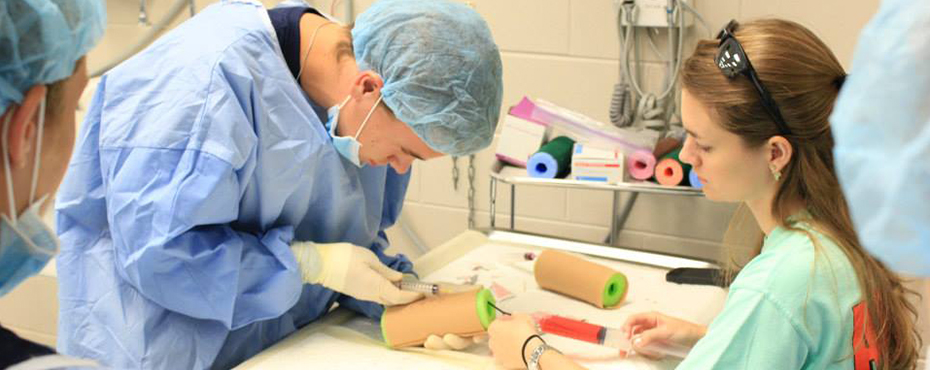 A student works with an instructor to practice drawing blood using a pool noodle for help.