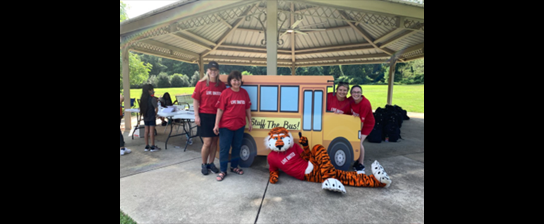 A group of volunteers posing for a picture under a gazebo with Aubie.
