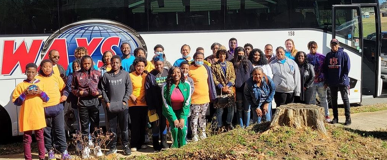 A group of students and mentors standing in front of a bus.