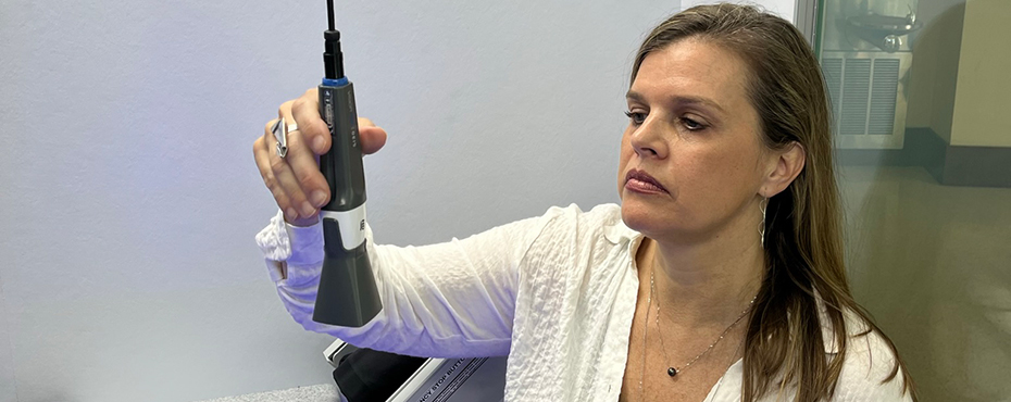 Woman sitting in telehealth station holds testing implement that is suspended from a cord.
