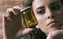 A woman staring at an unmarked bottle with pills inside with a contemplative look