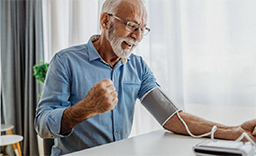 An older man using a blood pressure monitor on his left arm