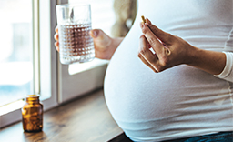 A Mid-stage pregnant woman taking supplements with a glass of water